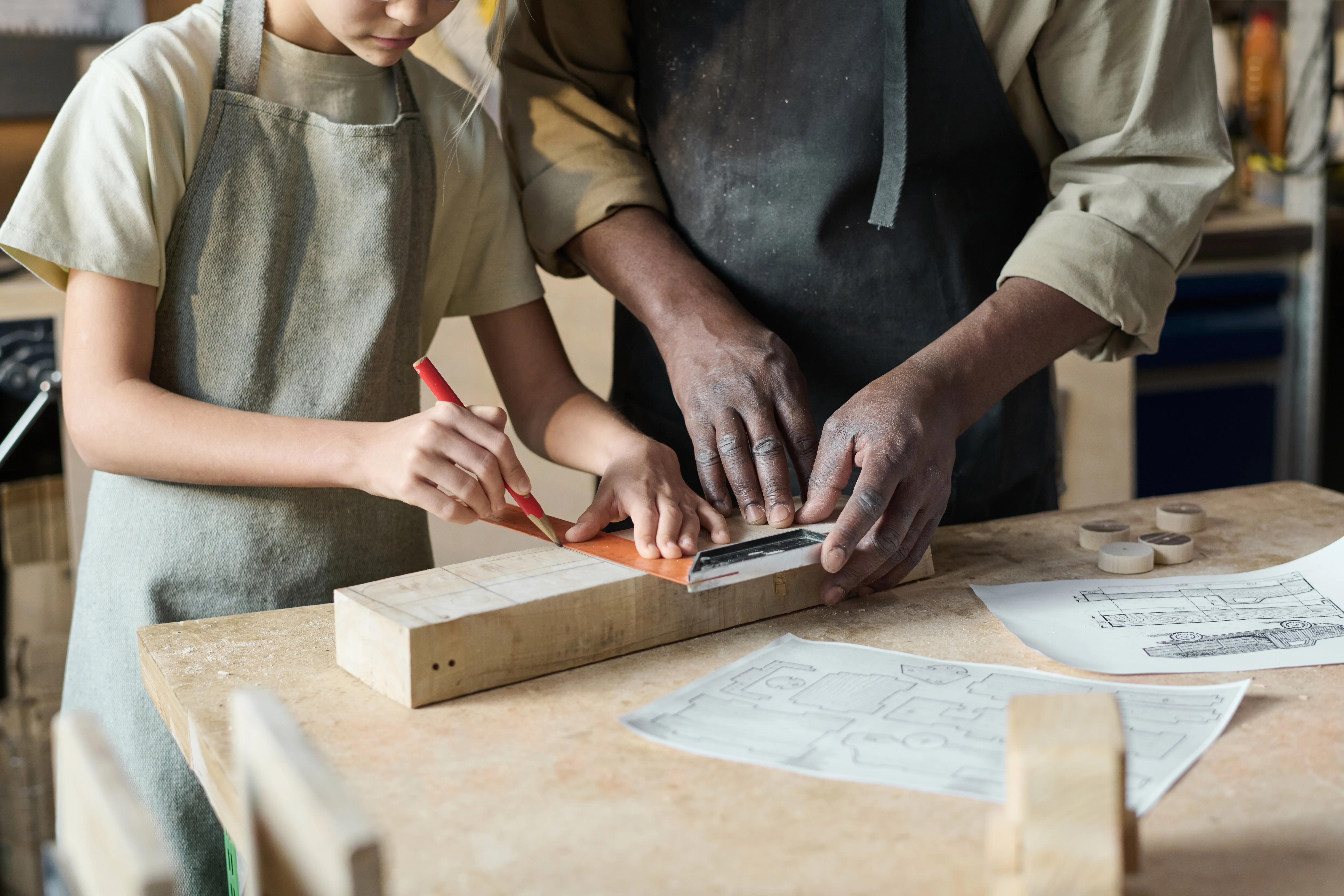 Älterer Tischler unterrichtet ein kleines Mädchen im Holzhandwerk in einer Handwerksschule für Kinder.